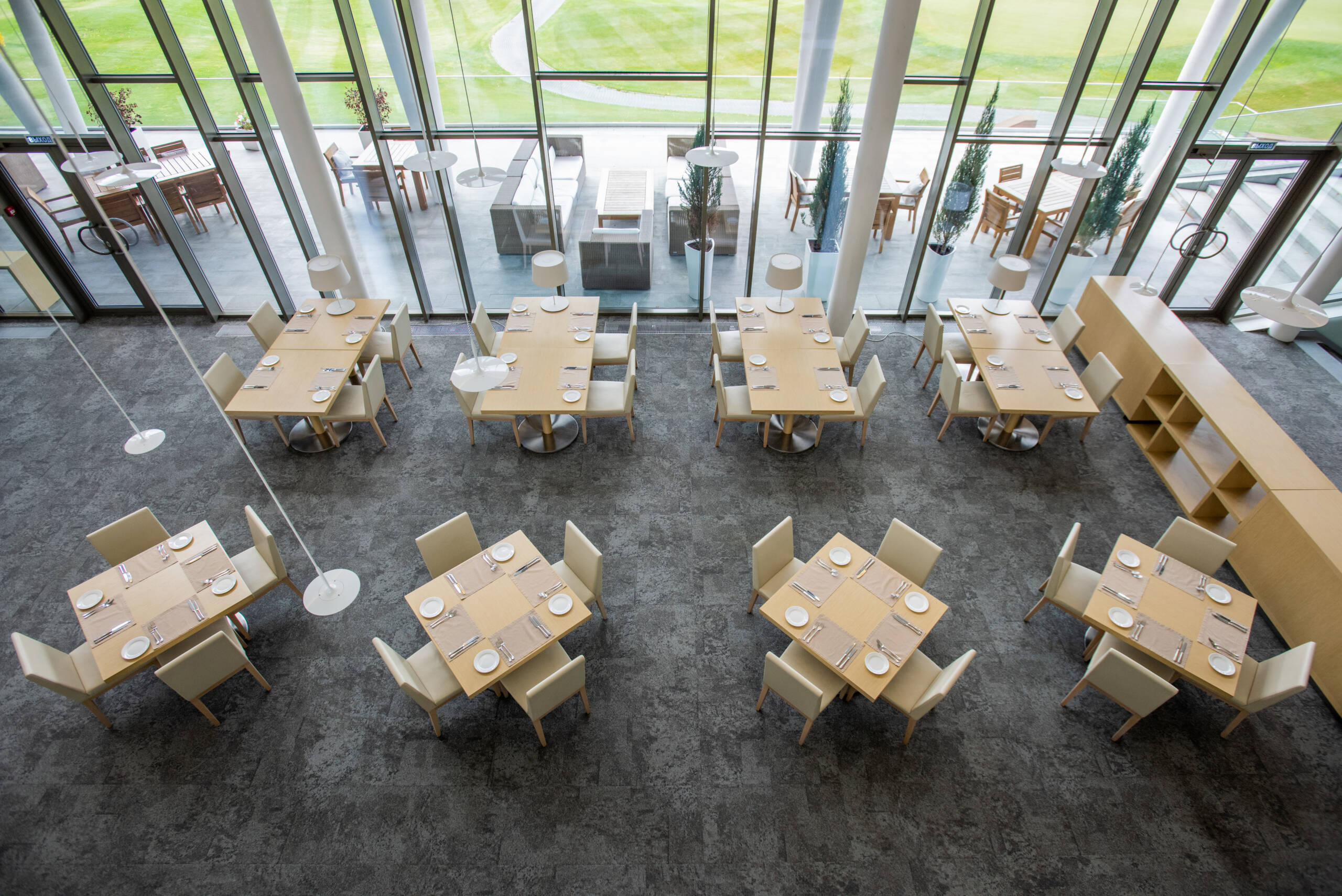 Overview of two rows of tables served for guests in large luxurious restaurant of business center situated in natural environment