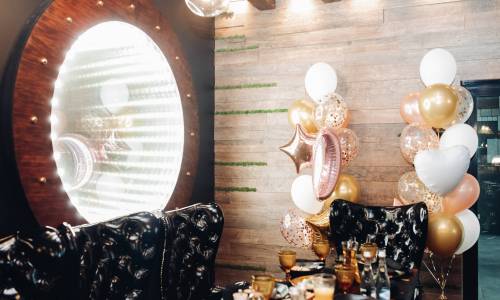 Black armchairs by the table and large illuminated mirror on the wall. Foiled balloons by the wall. Party concept