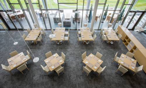 Overview of two rows of tables served for guests in large luxurious restaurant of business center situated in natural environment