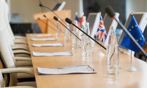Political reports in clipboards placed on conference table with glass bottles, national flags and microphones